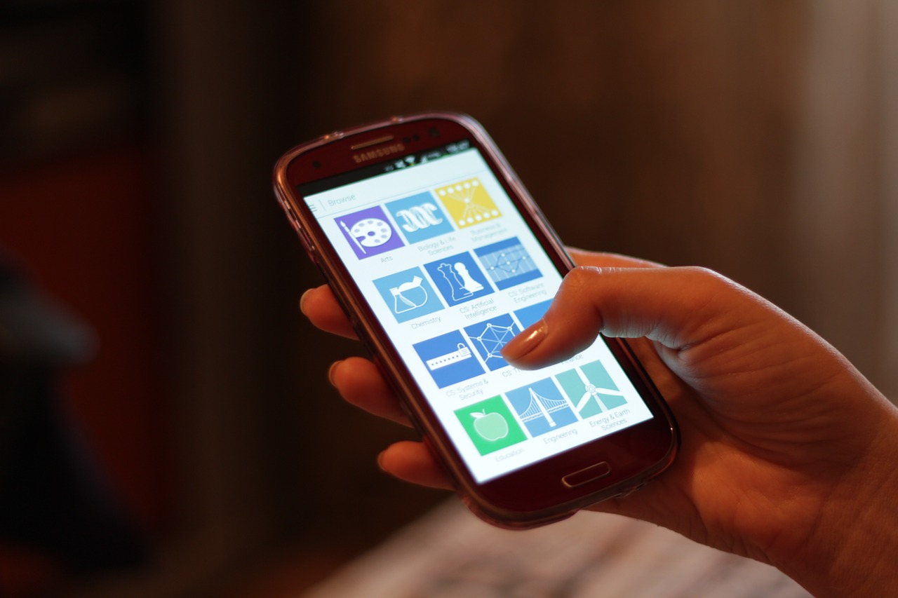 A hand holding a smartphone displaying its home screen
